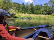  Kind sitzt in einem Kanu auf einem Fluss, im Hintergrund paddelt eine weitere Gruppe in einem zweiten Boot.