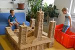 Zwei Kinder bauen aus Holzplättchen eine große Struktur mit Türmen und Mauern im Spielzimmer.