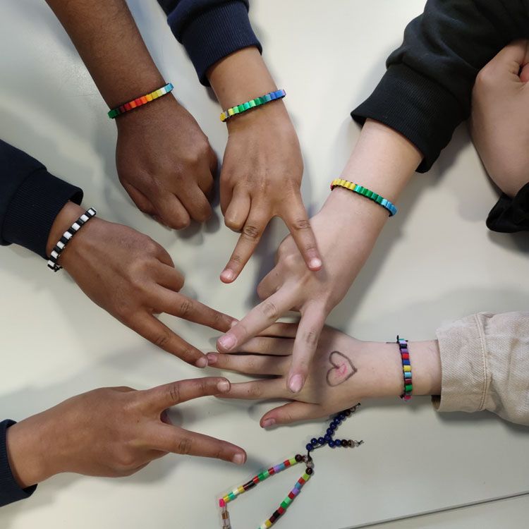 Mehrere Hände mit bunten Perlenarmbändern liegen auf einem Tisch, eine Hand zeigt ein gezeichnetes Herz.