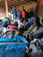 Gruppe von Kindern sitzt in einer Holzhütte um einen Tisch, davor liegen viele Rucksäcke und Taschen.